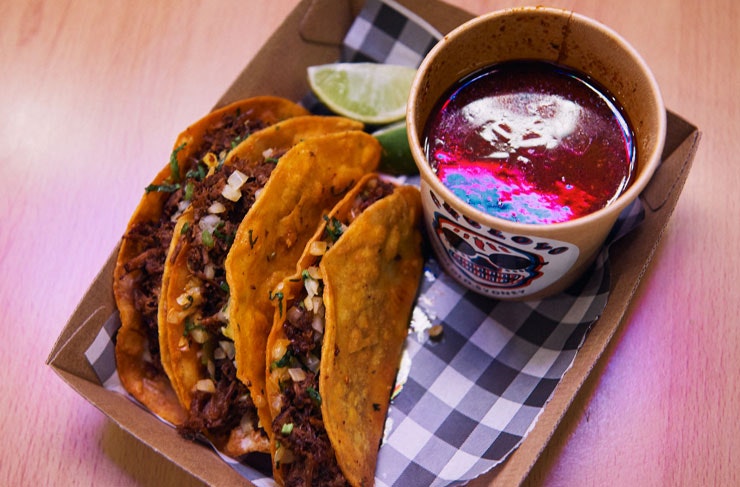 Birria tacos served on white and black check paper with a slice of lime.